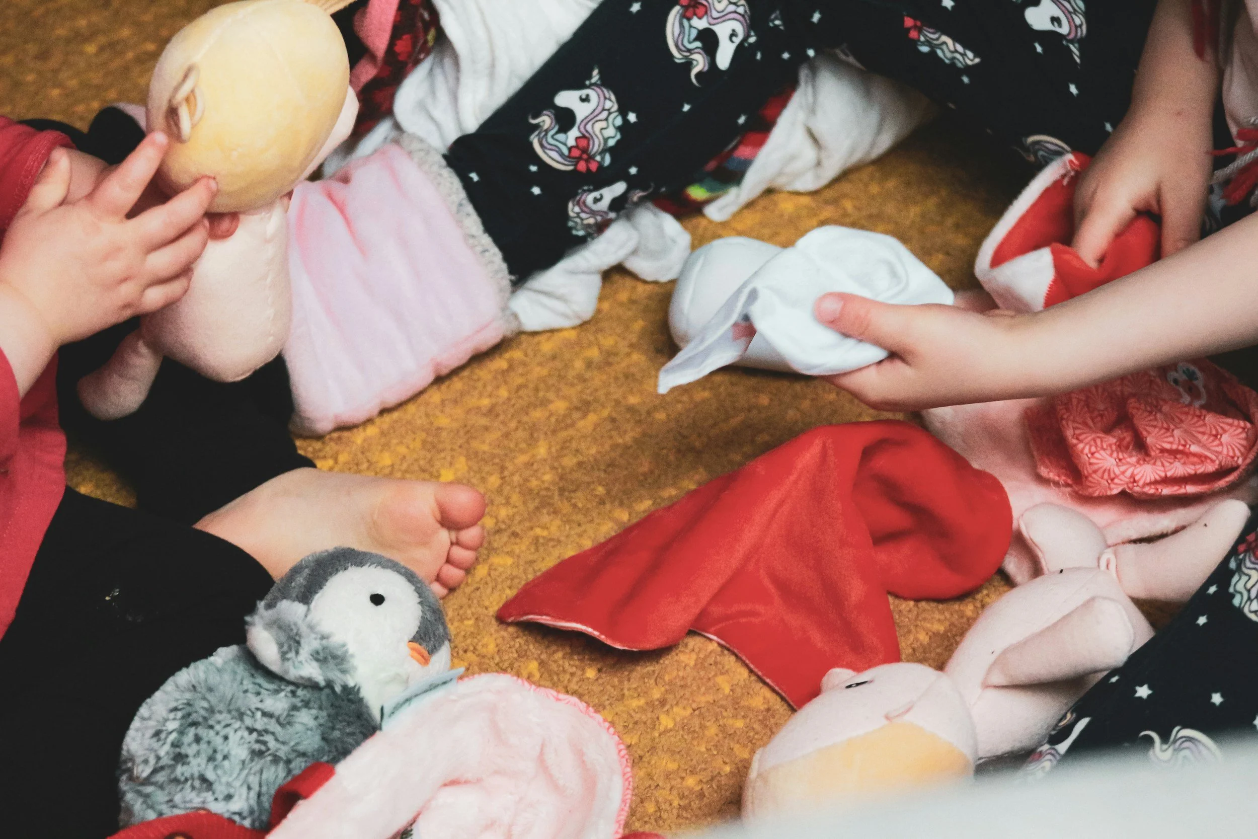 Children's hands reaching for plush toys and socks on a carpeted floor, with stuffed animal toys including a penguin and a mouse, and various colorful socks a showing of distributing clothes and toys to child victims of trafficking
