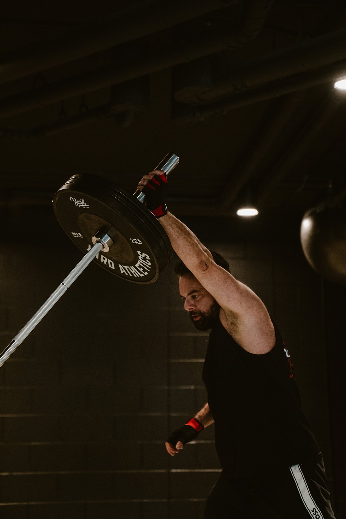 A man lifting a barbell overhead in a gym or workout space.
