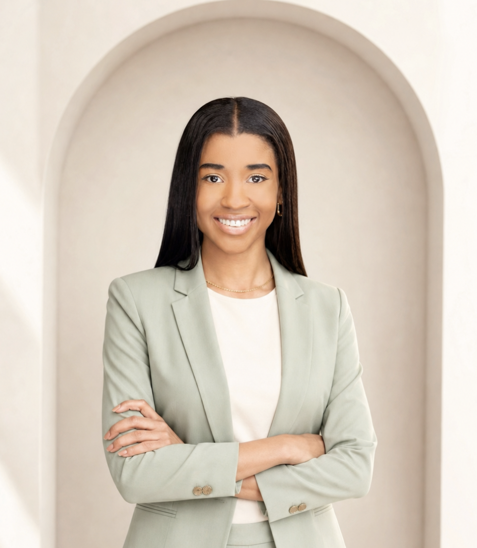 A young woman with long black hair, wearing a light green blazer and white top, standing with arms crossed in front of a neutral background with an arched opening.