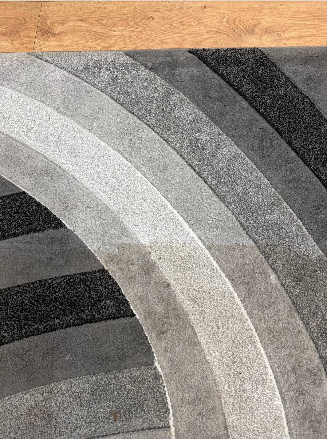 Close-up of a circular patterned rug with curved stripes in shades of gray, black, and white, on a wooden floor.
