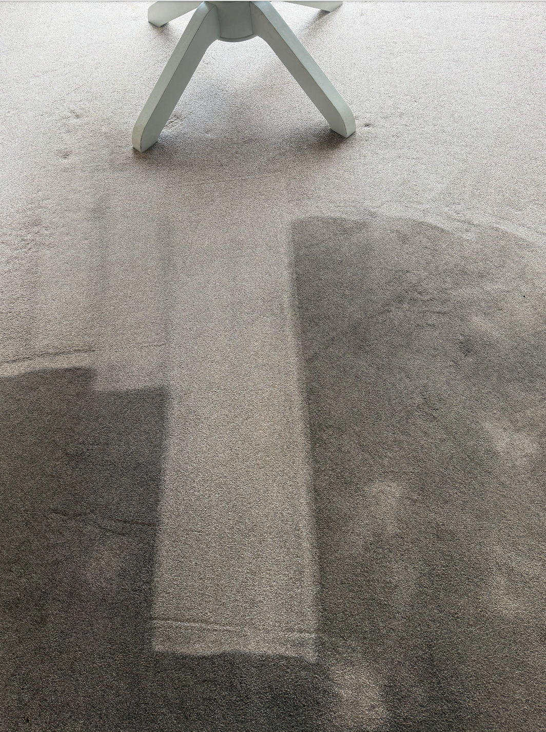 A white chair with angled legs is standing on a carpeted floor, casting a shadow.
