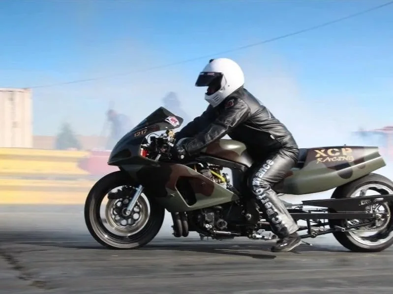 A person in a white helmet and black leather suit riding a racing motorcycle on a racetrack.
