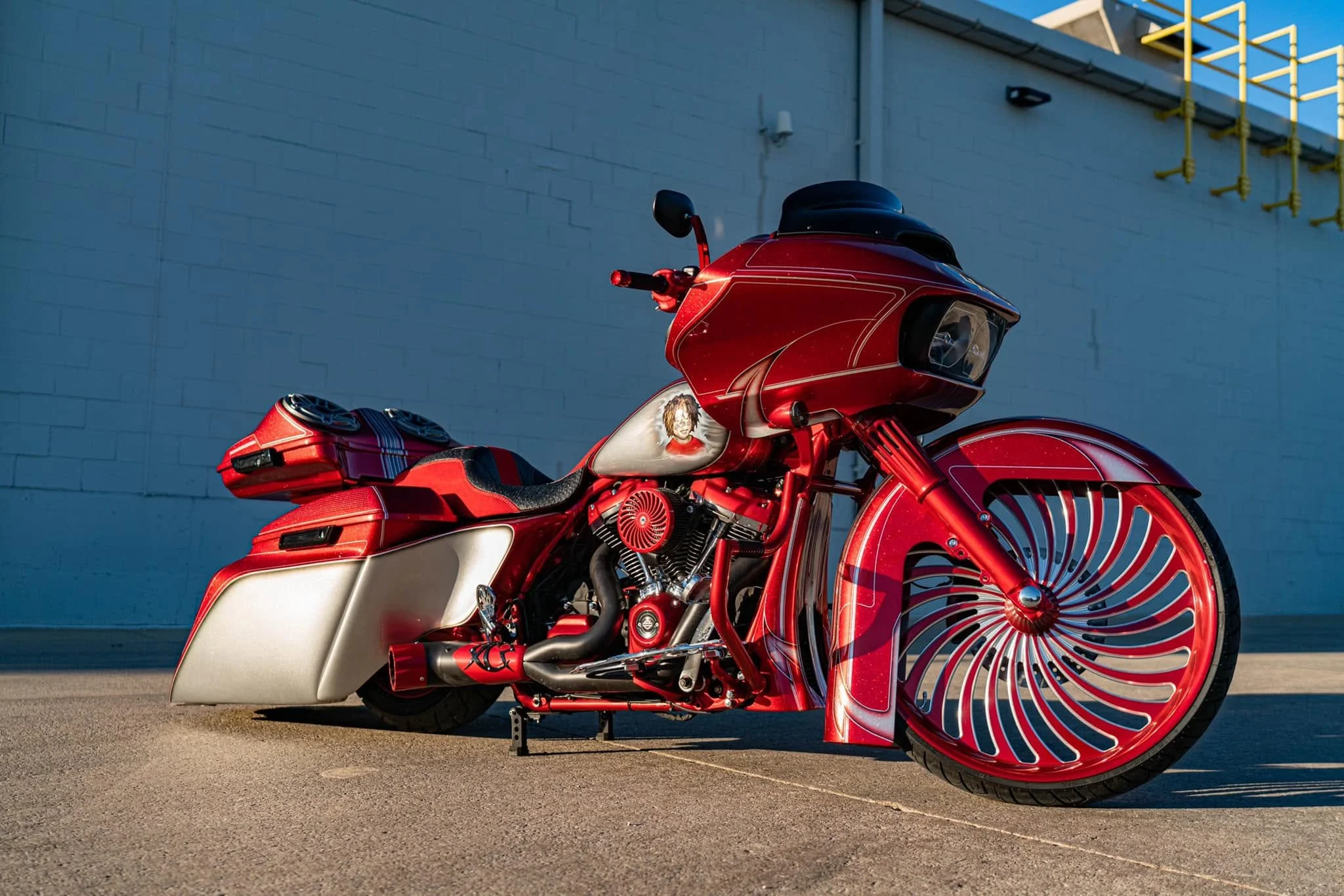 A red motorcycle with unique wheel designs parked outdoors near a white building with yellow safety railings.