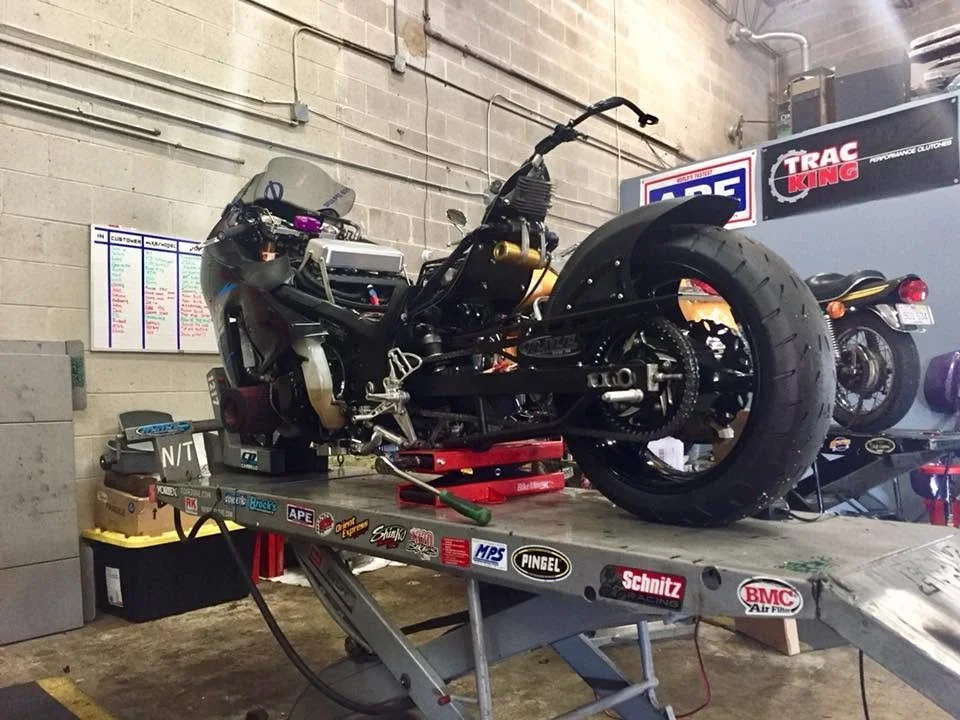 A motorcycle under repair on a workbench in a garage, with parts removed.