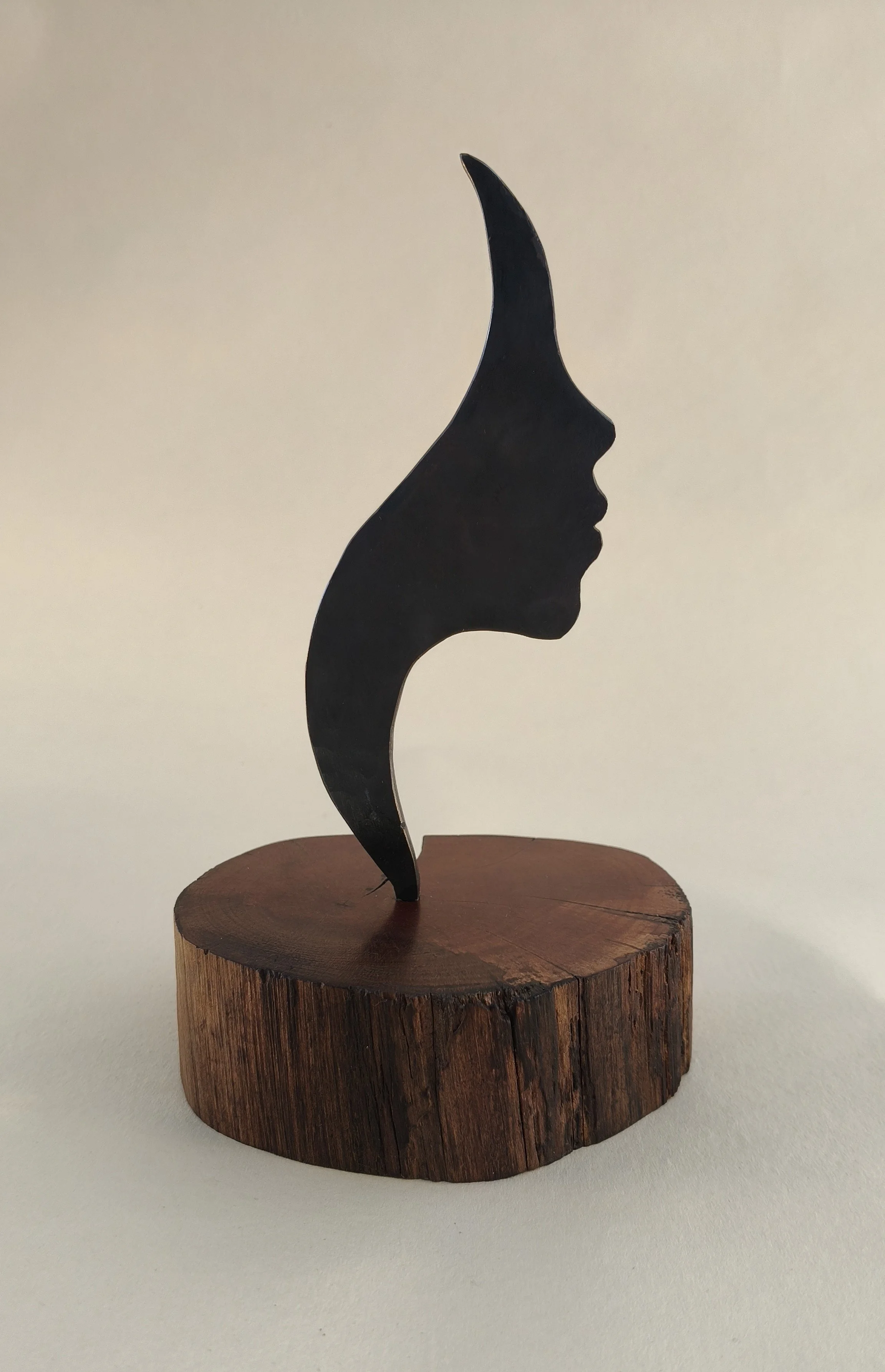 Sculpture of a profile of a human face with a horn-like extension, mounted on a wooden base.