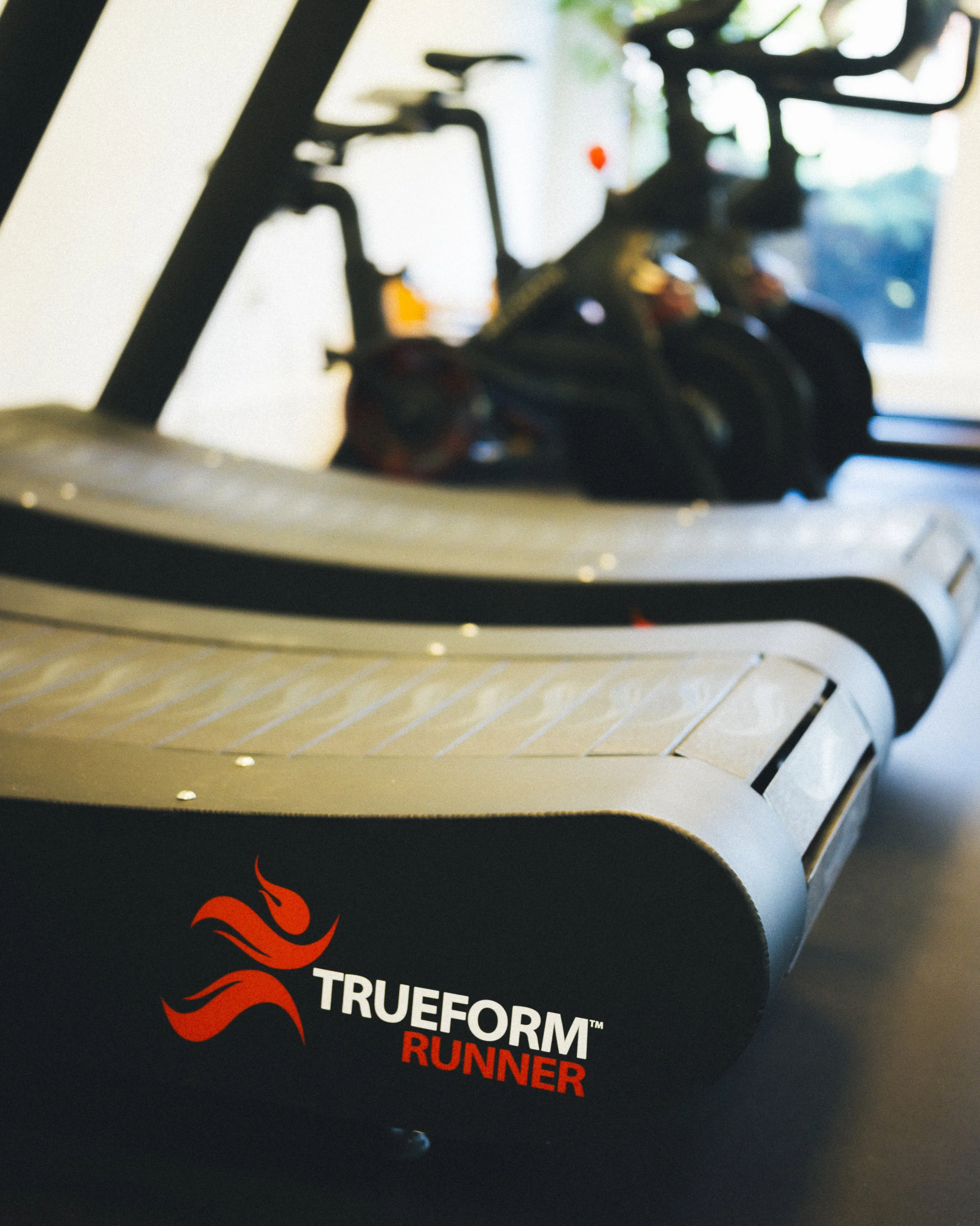 Close-up of a black box with red flame graphic and white text reading 'TRUEFORM' and red text reading 'RUNNER', featuring two black and orange running shoes on top.