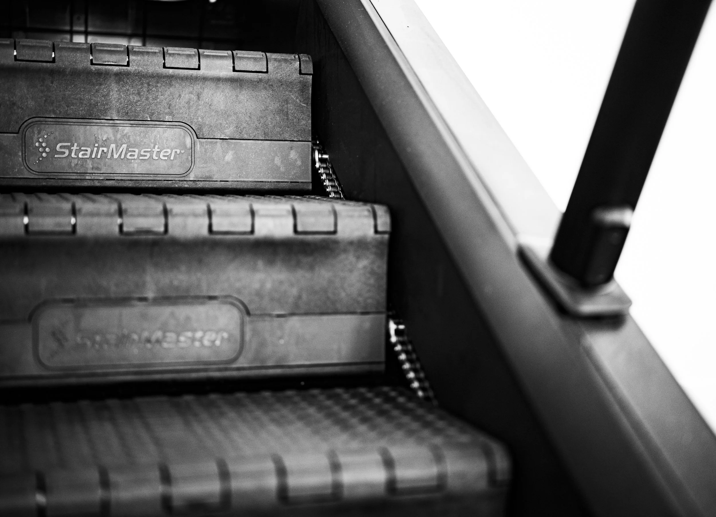 Close-up of a stair tread with a label 'StairMaster' on it, part of a stairway or fitness equipment, in black and white.