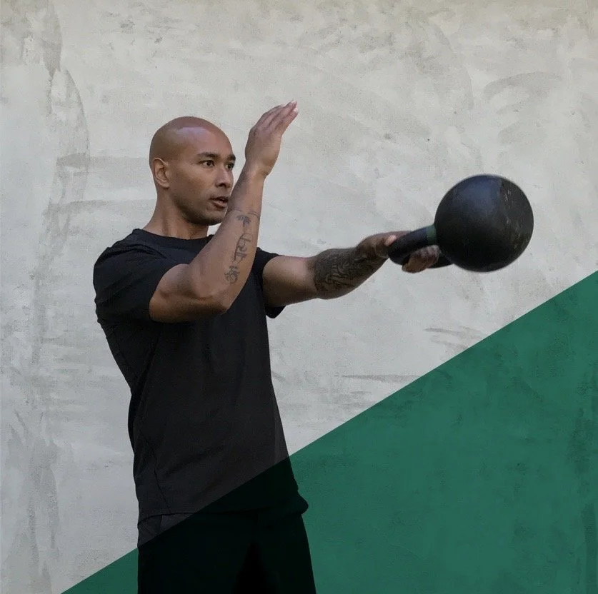 A man in black workout clothes is performing a kettlebell exercise against a plain wall