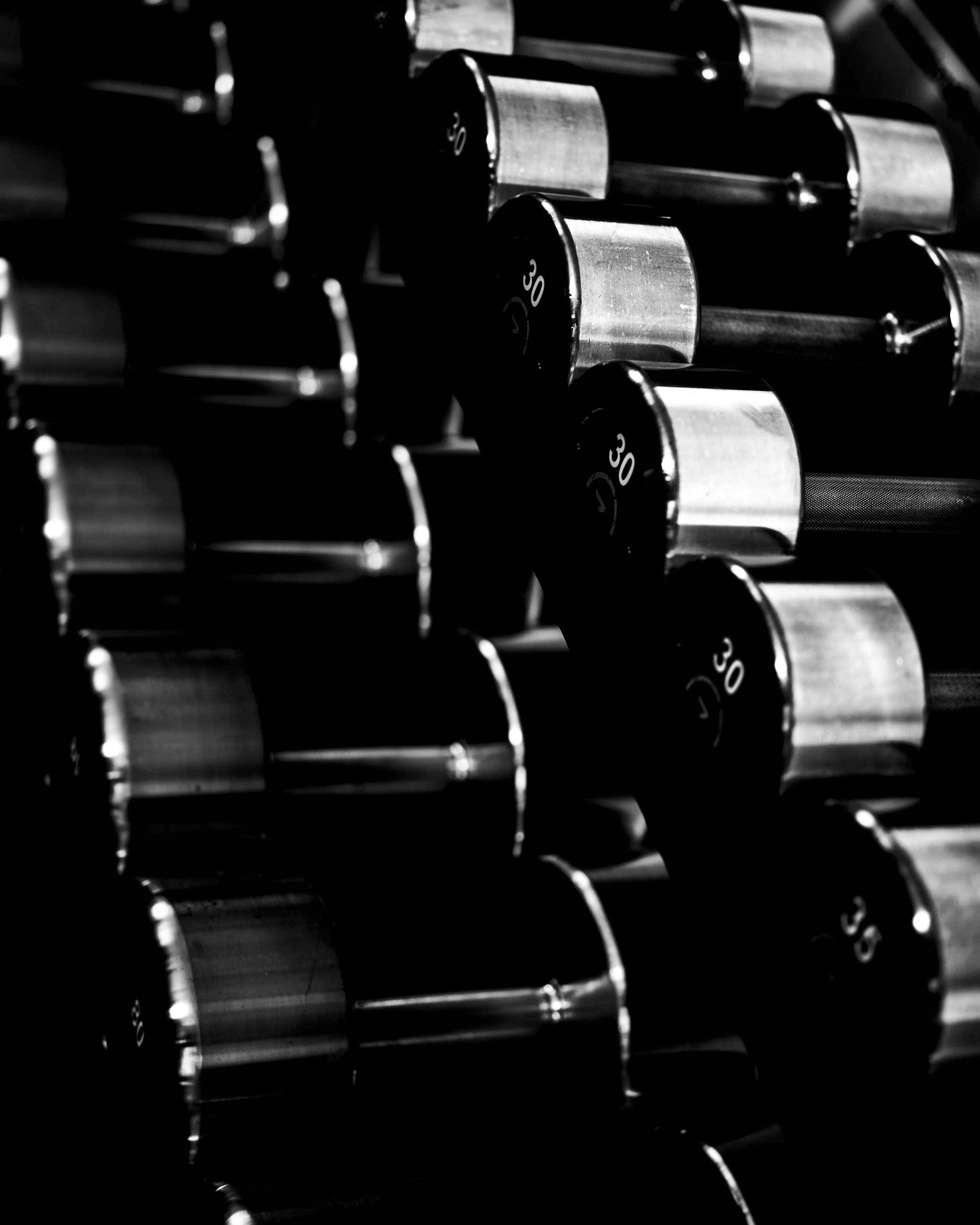 Close-up of black dumbbells with silver handles and white weight markings stacked in a gym or fitness setting.