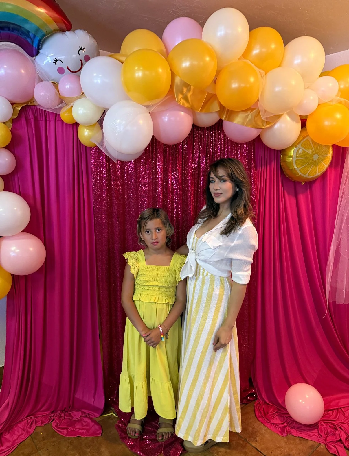 Yazmine Enriquez, 2026 Kerman Mayor Candidate and a young girl standing in front of a pink and gold balloon backdrop with a pink sequin curtain.