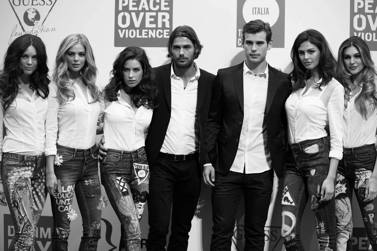 Group of seven young adults, three men and four women, standing together in front of a backdrop with logos and slogans related to peace and anti-violence.