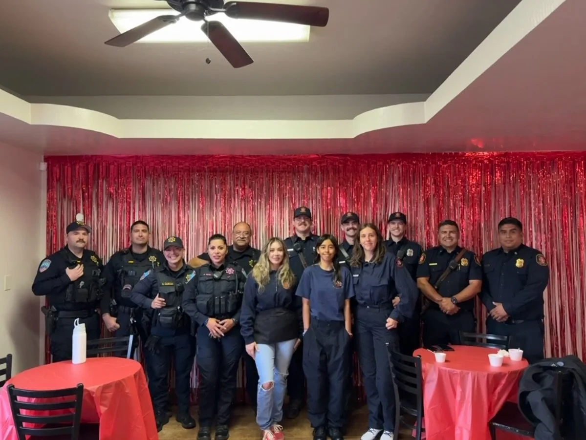 Group of police officers and two women standing together in a room with red curtains and red tablecloths.