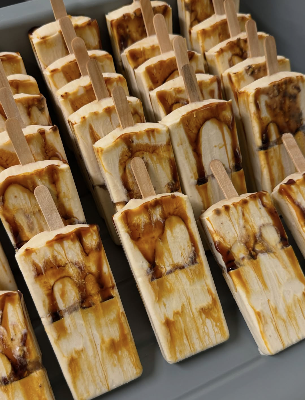 Multiple banana caramel popsicles with caramel swirls and drizzles, arranged in rows.