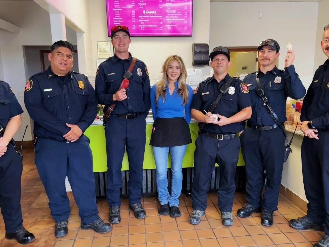 Yazmine Enriquez, 2026 Kerman Mayor Candidate and police officers standing together in a restaurant, smiling at the camera. The woman is wearing a blue shirt and black apron, while the officers are in navy blue uniforms.