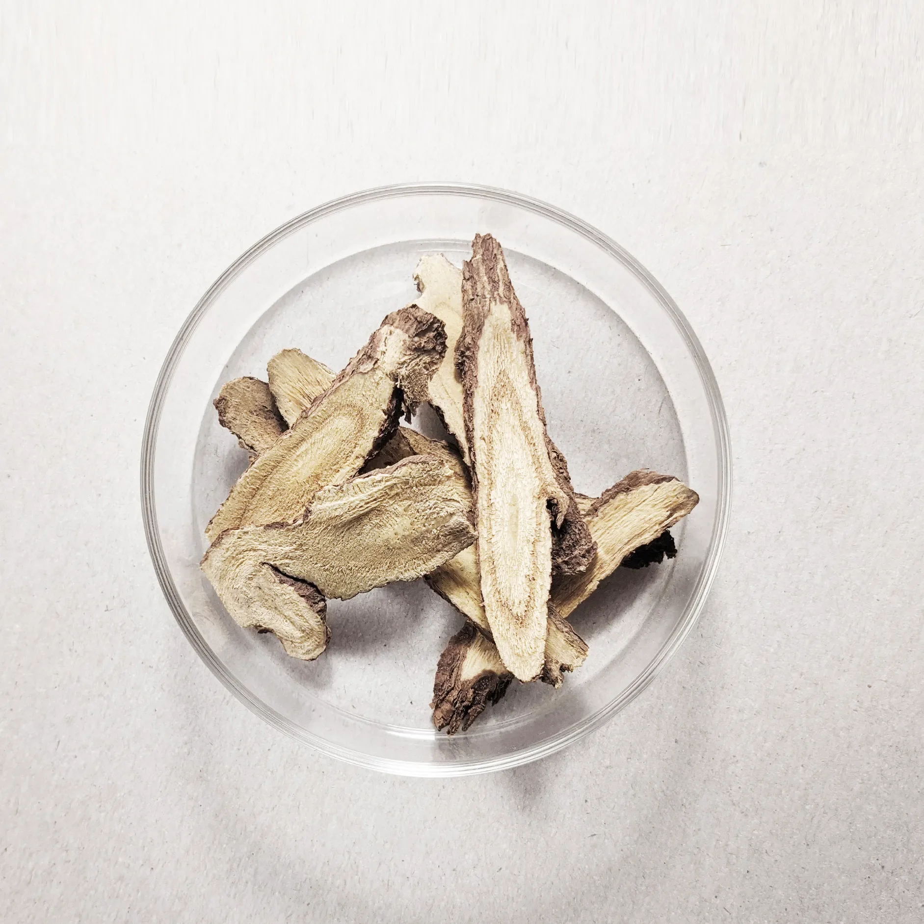 Clear glass bowl filled with sliced dried ginger on a white surface.