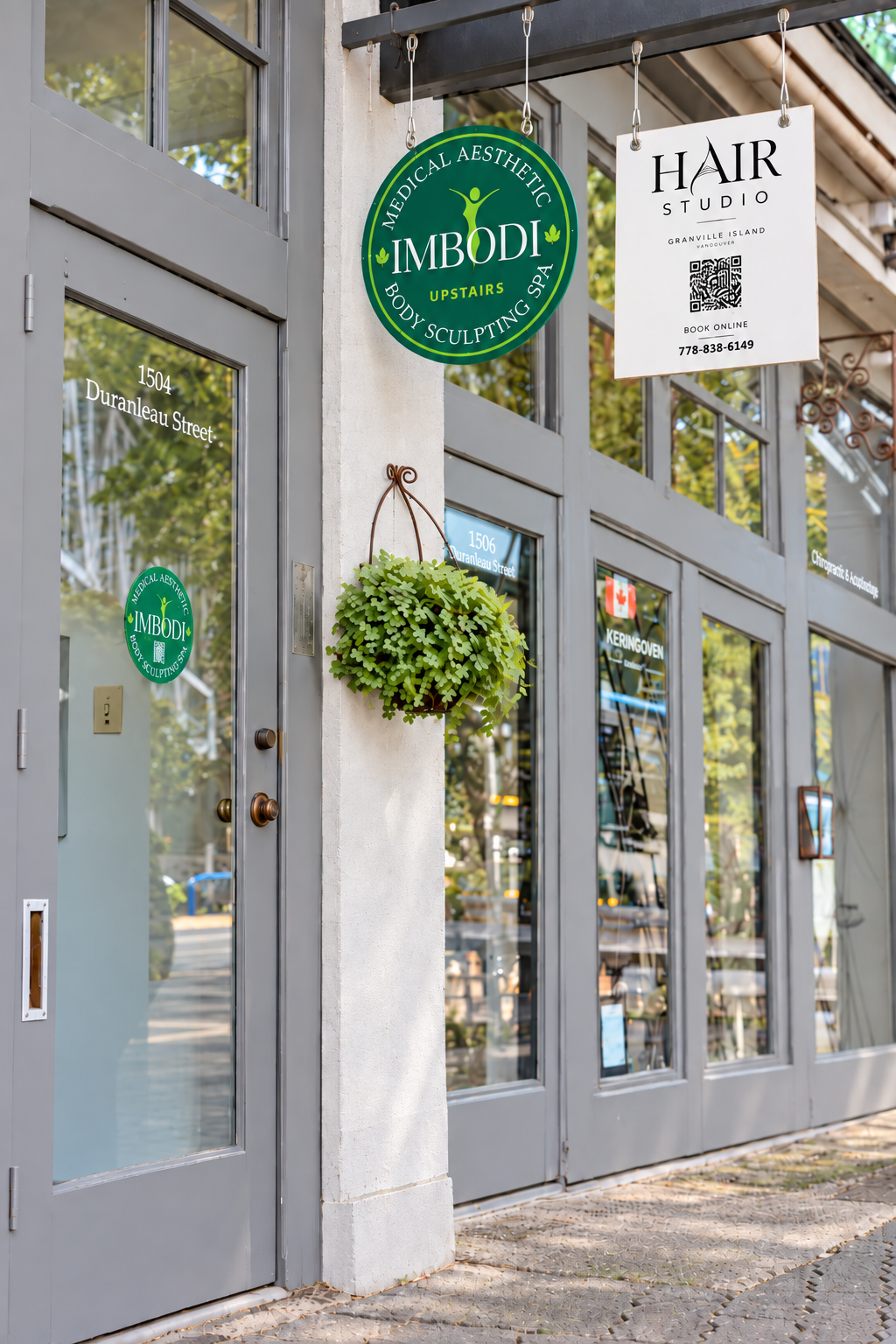 Exterior of a storefront with signs for 'IMBODY Medical Aesthetic & Body Sculpting Spa,' a hair studio, and a hanging potted plant.