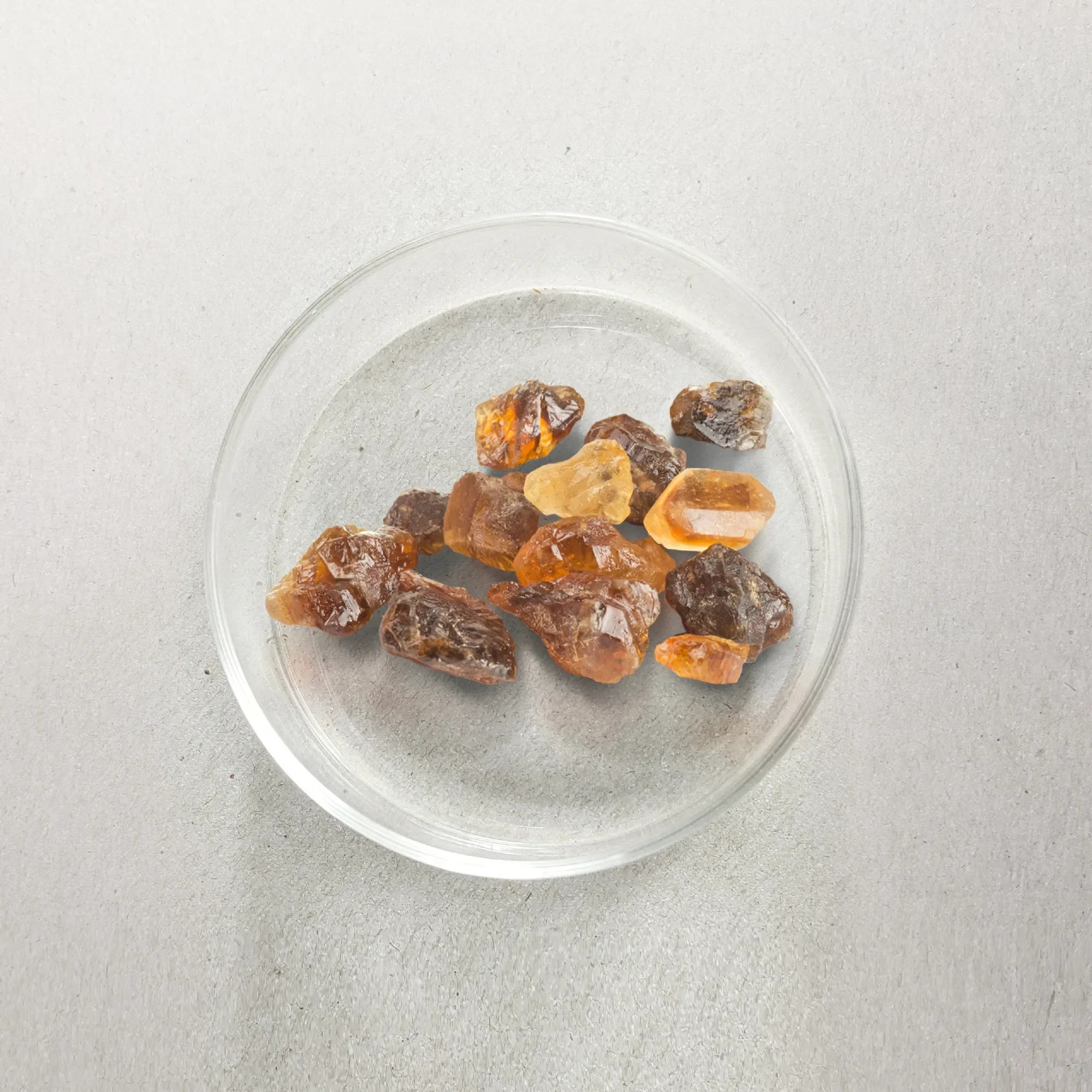 Assorted raw gemstones on a transparent dish placed on a gray surface.