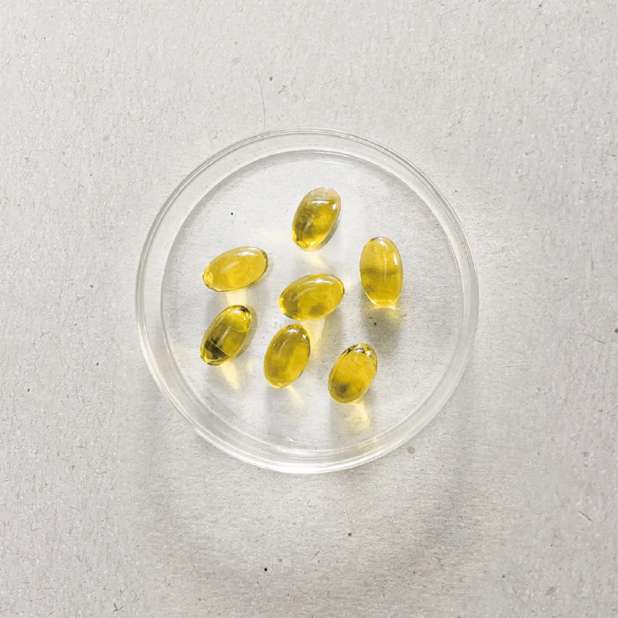 Small yellow capsules in a clear plastic container on a gray surface.