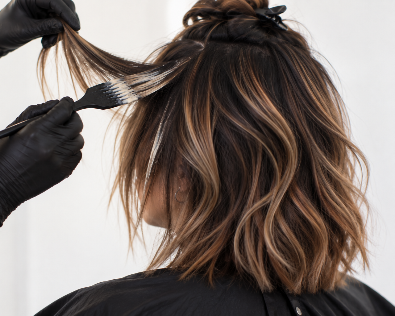 Hairdresser applying highlights to a woman's hair with a comb and foil.