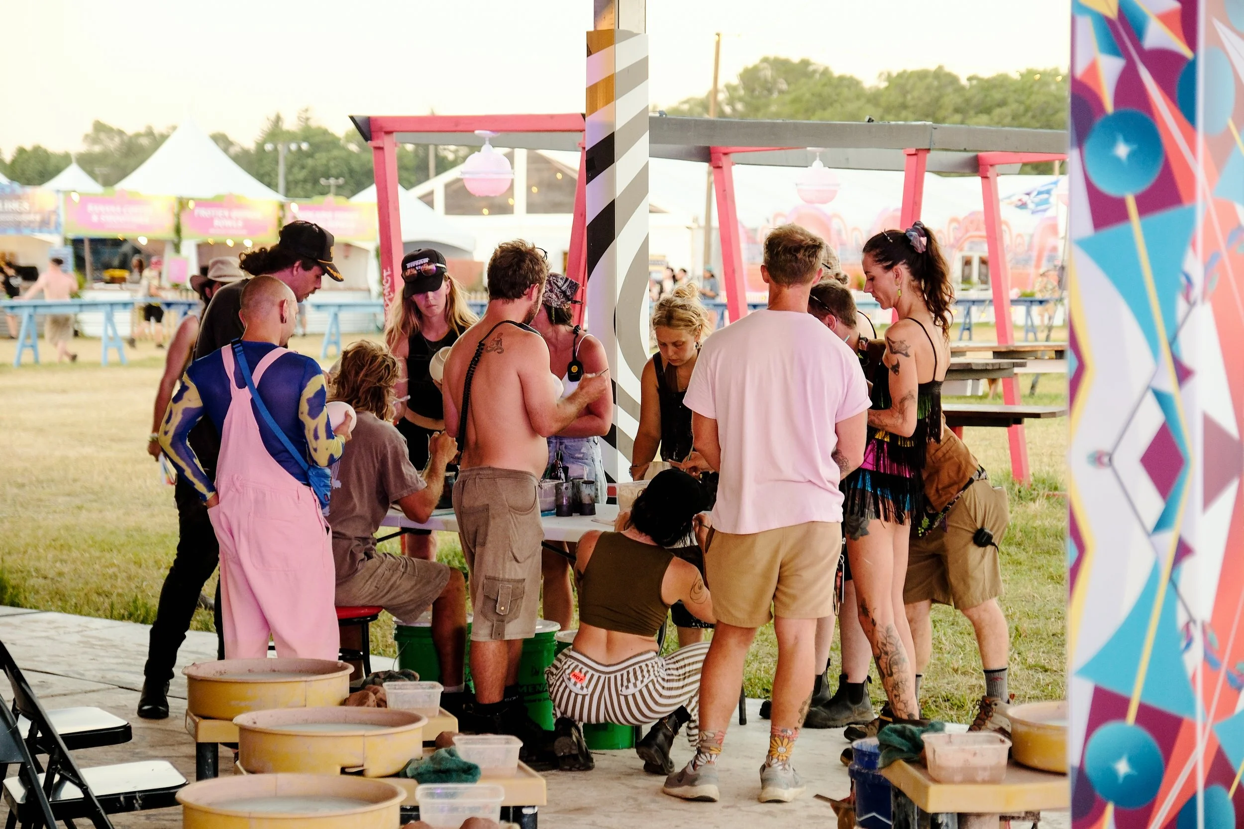 People gathering at a colorful outdoor festival art booth with painted decorations and supplies.