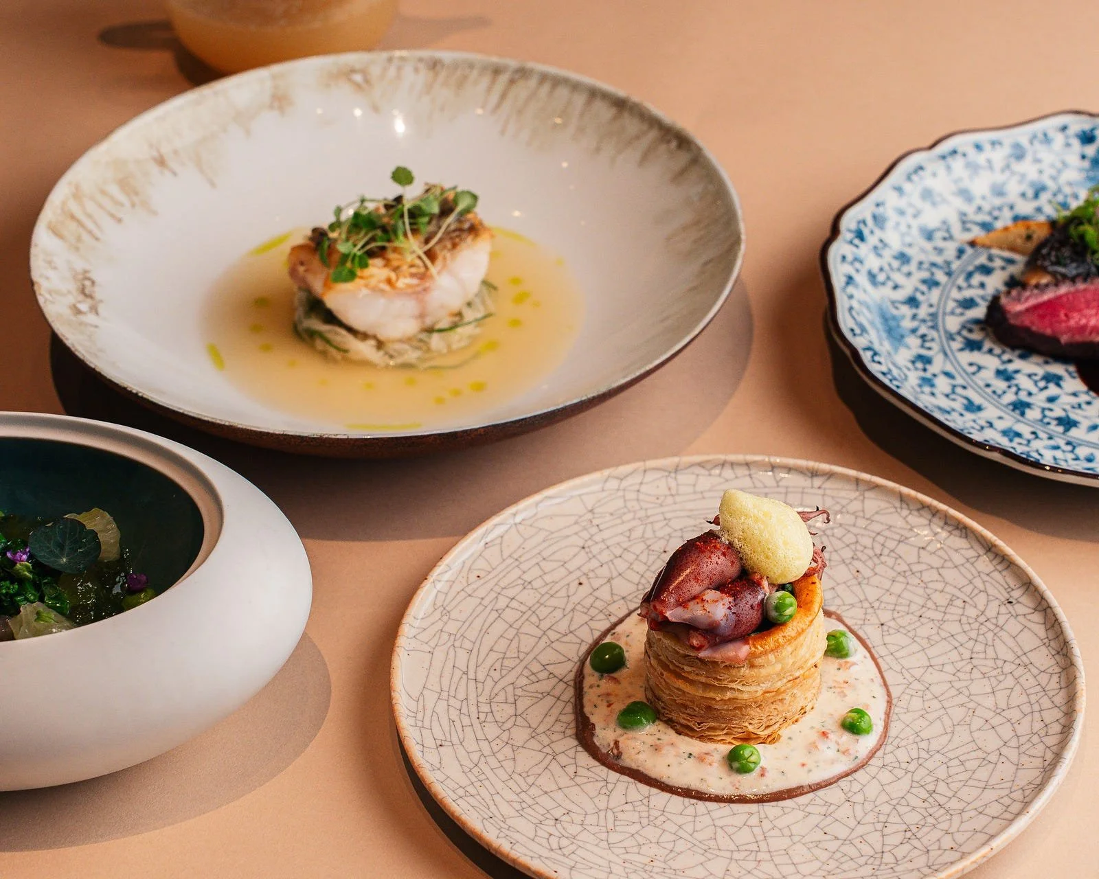 Four elegantly plated dishes arranged on a table in an upscale fine-dining restaurant.