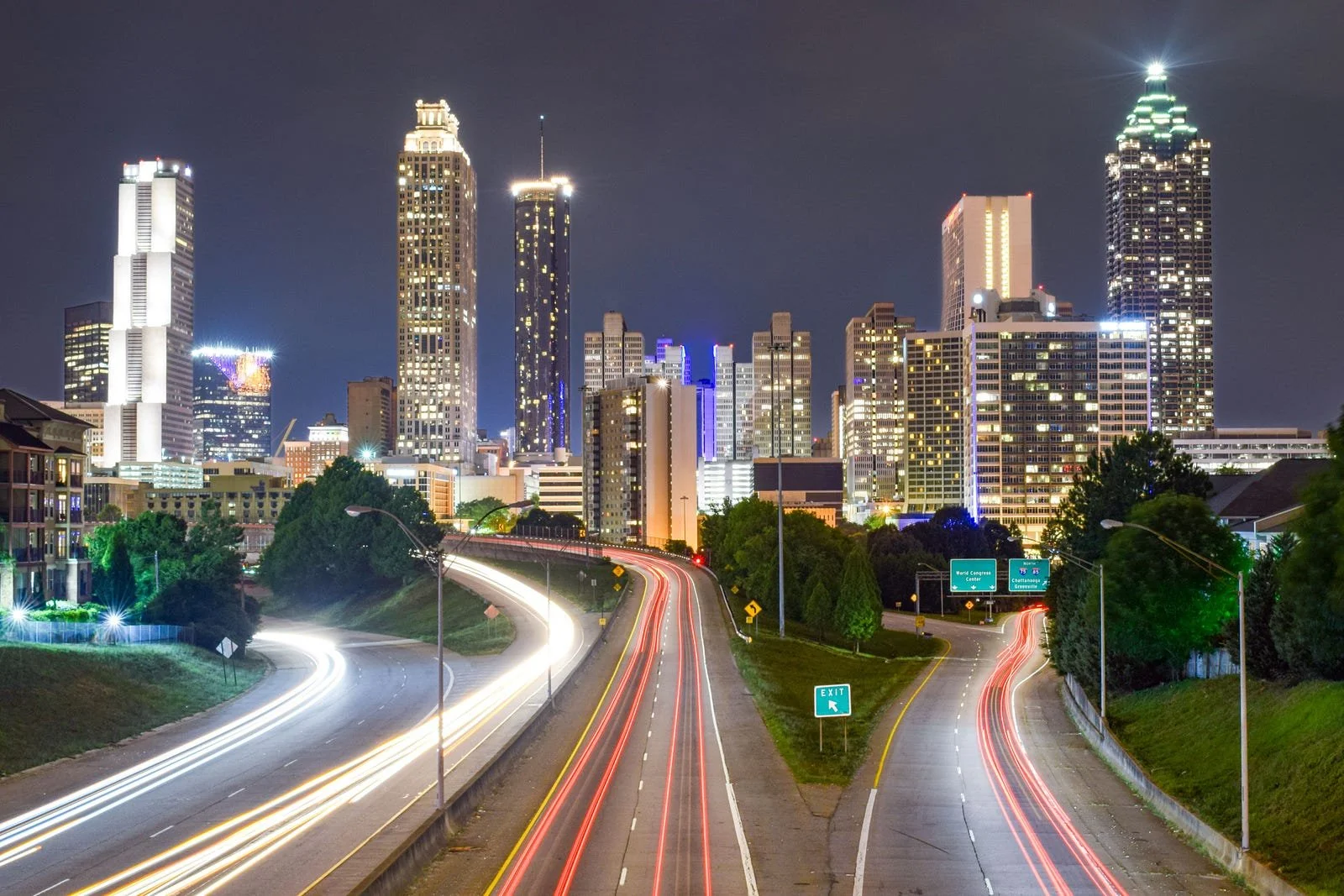 Atlanta skyline illuminated at night as the expressway leads into the city, with downtown buildings visible in the distance.