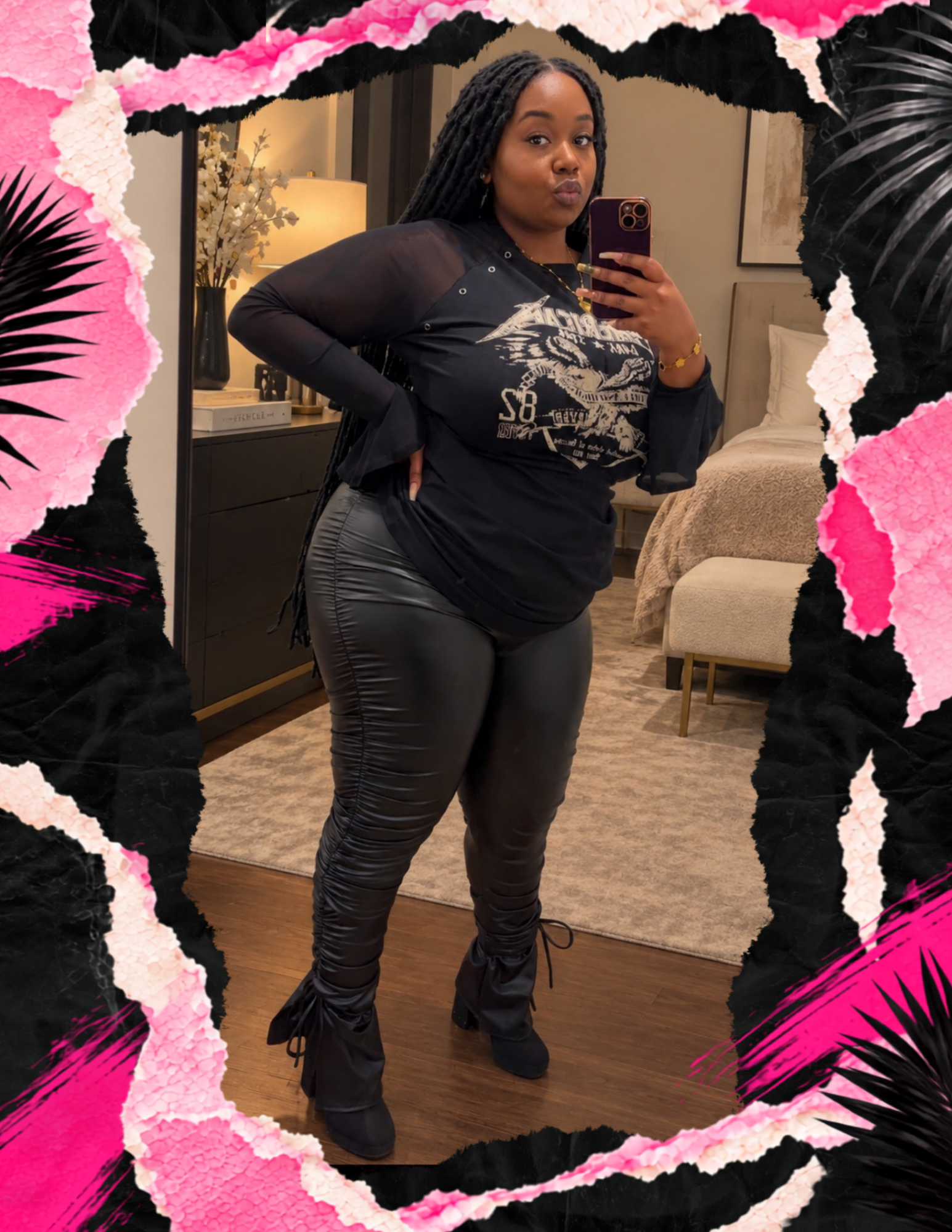 A woman taking a mirror selfie in a hotel room, wearing a black graphic long sleeve top and shiny black pants with lace-up front, surrounded by a black, pink, and white textured floral border.