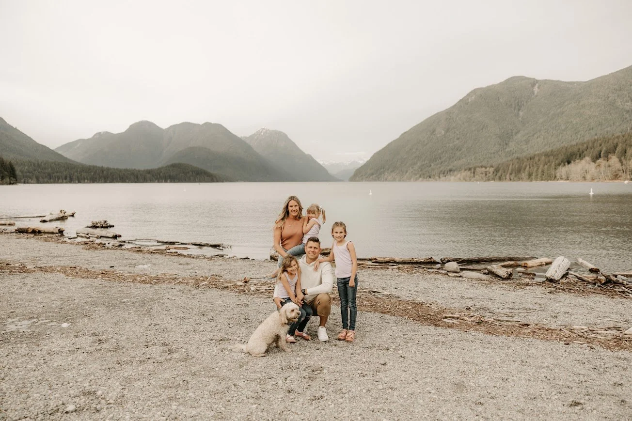Family of five with a dog by a lake surrounded by mountains