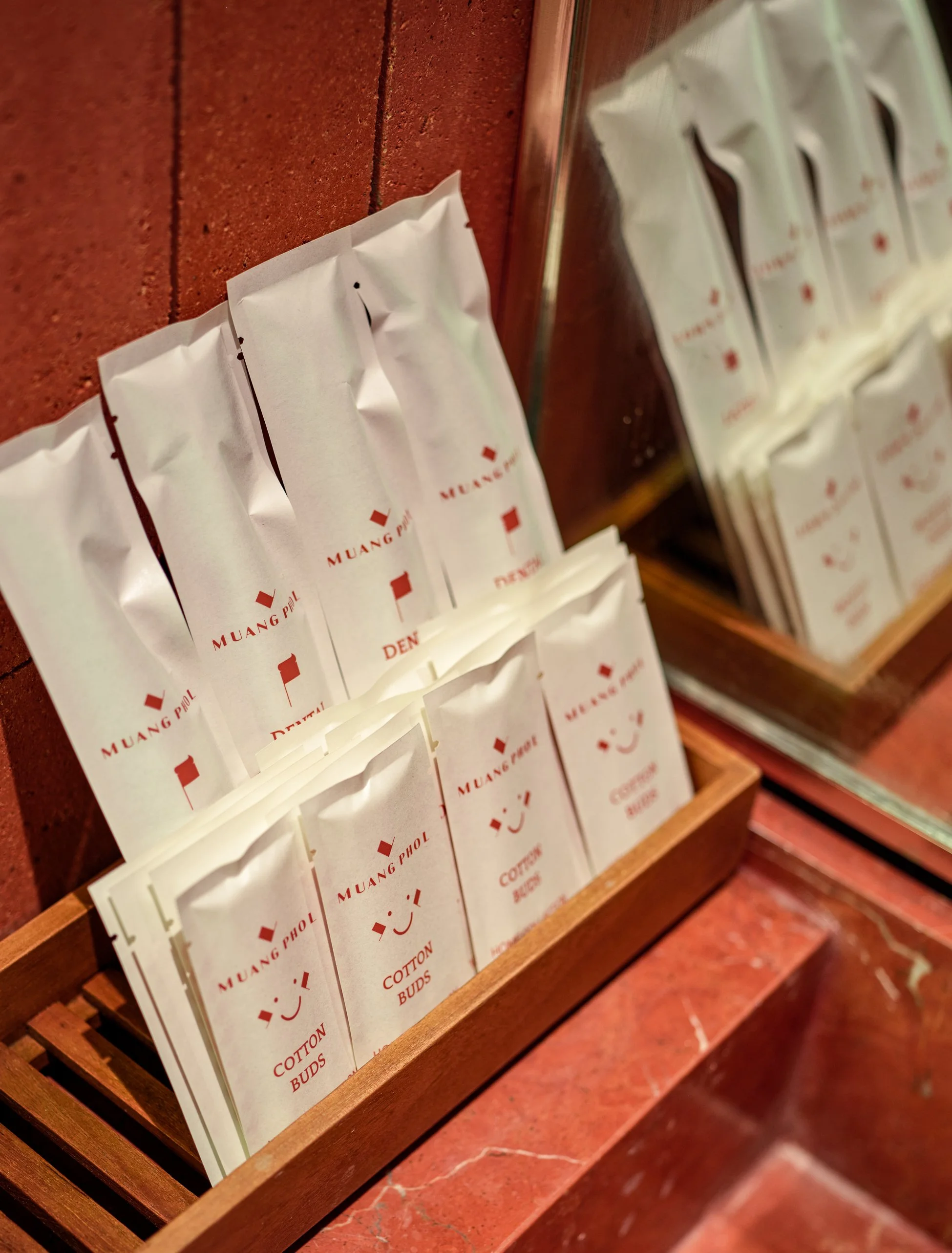 Packets of sugar labeled 'Muang Phol' and other sugar-related items in a wooden display shelf against a brick wall.