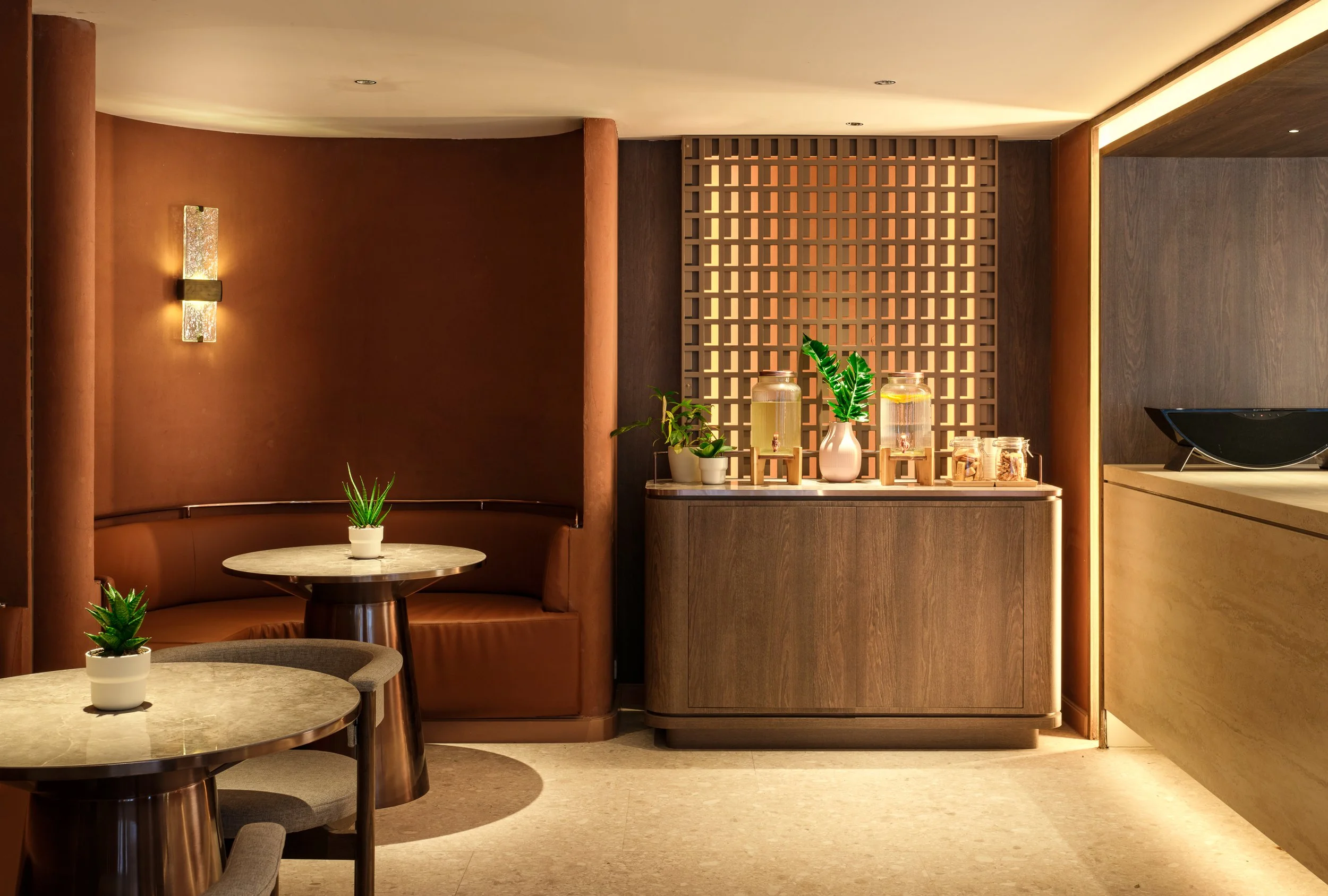 A cozy interior of a restaurant or cafe with warm lighting, decorative wall sconce, wooden lattice partition, and tables with potted plants.