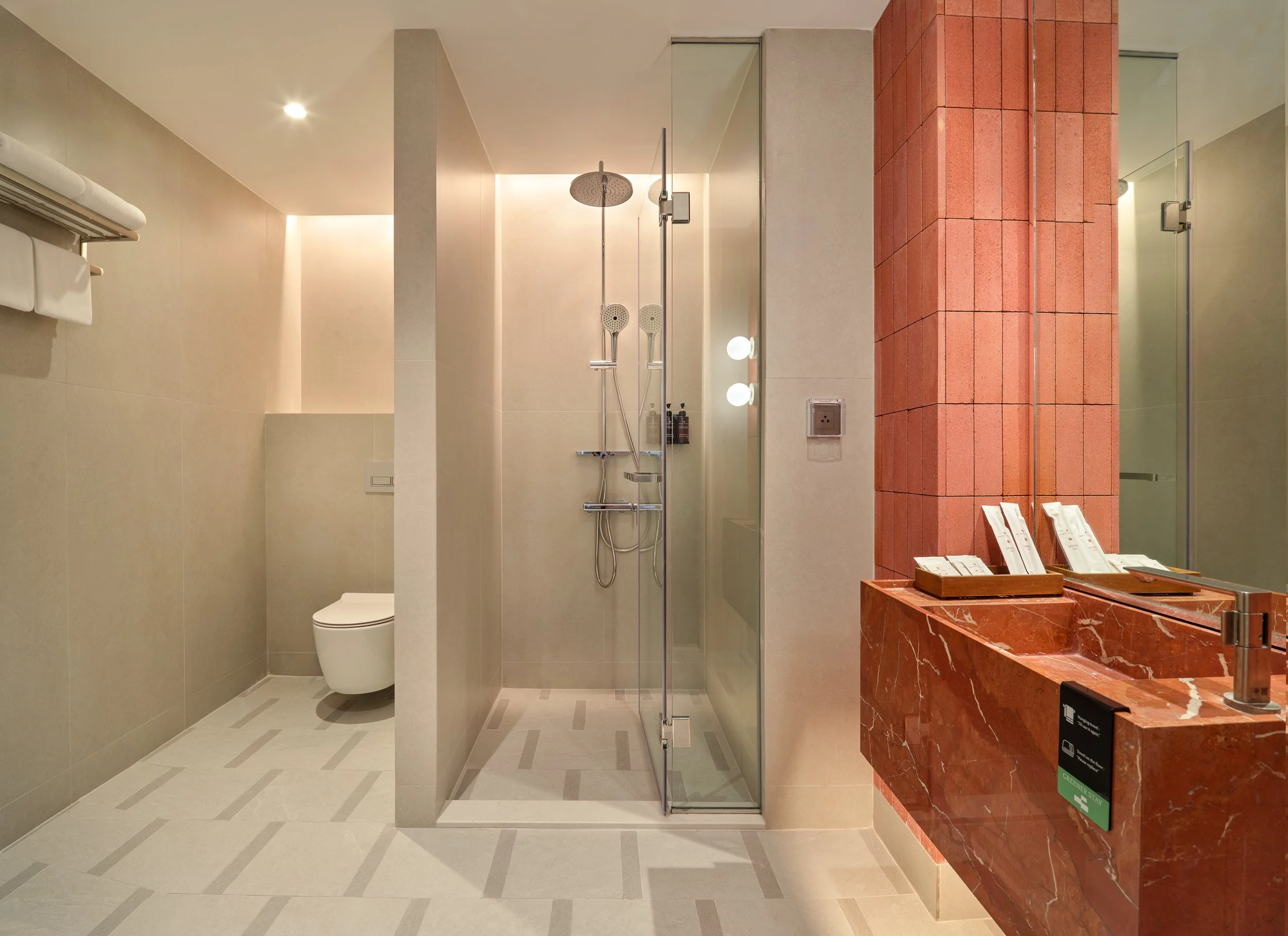 Modern hotel bathroom with a walk-in shower, a toilet, and a red marble vanity with a sink and mirror.