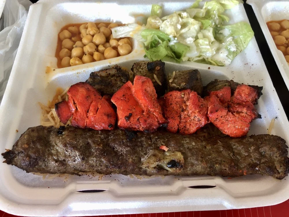 A takeout tray with grilled meat, grilled vegetables, chickpeas, and lettuce salad.