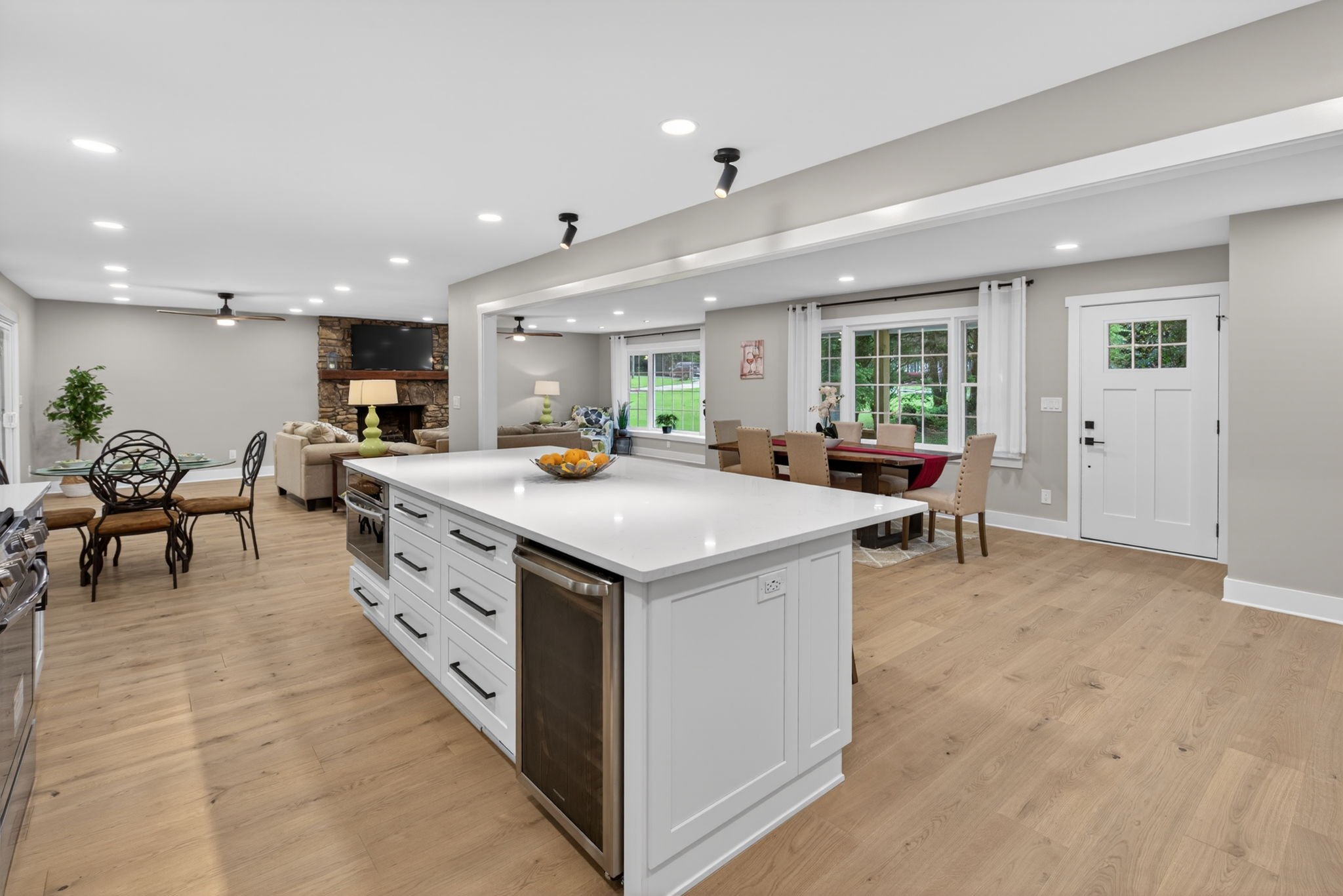 Open-concept living and dining area with a kitchen island, hardwood floors, and large windows showing a yard outside.