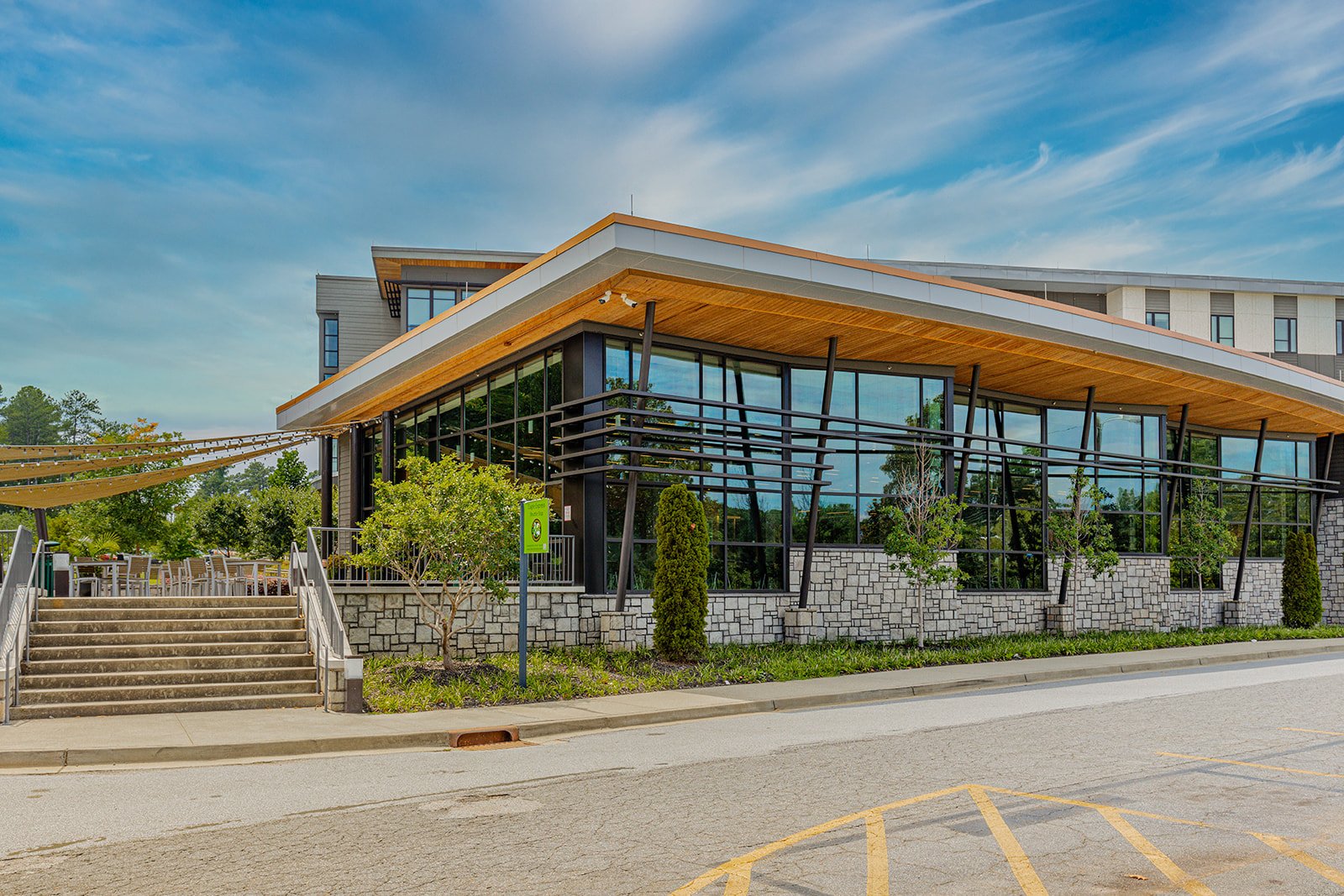 Modern restaurant or cafe building with large glass windows, outdoor seating, and landscaped surroundings under a blue sky.