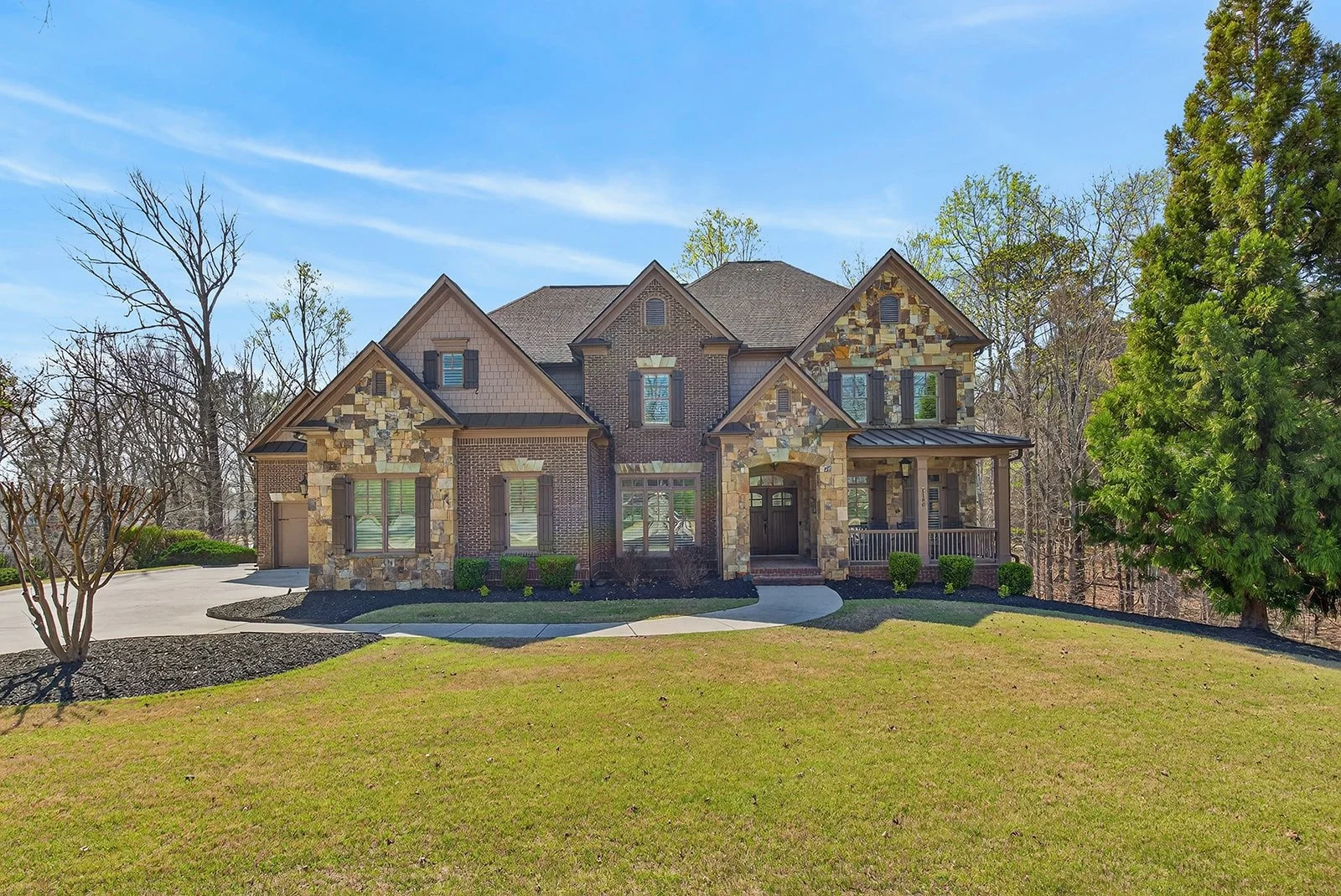 Front view of a large, two-story house with stone and brick exterior, surrounded by a well-maintained lawn and trees.