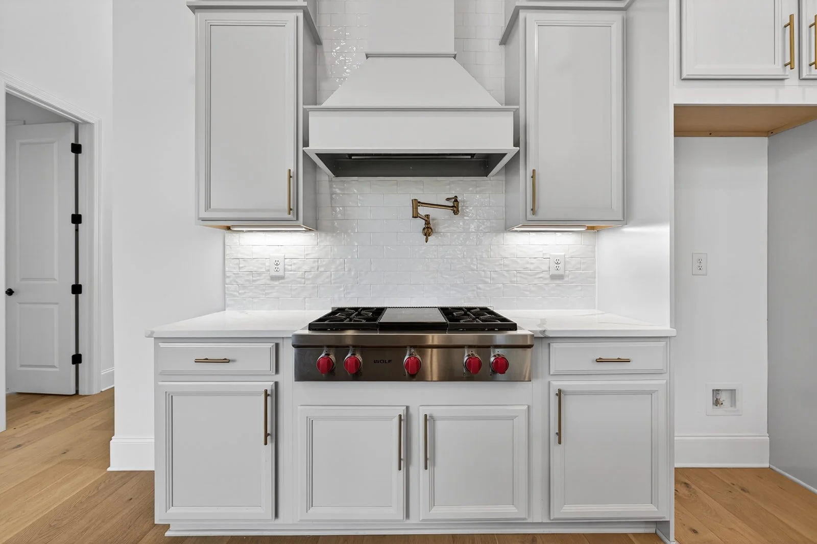 Kitchen with white cabinets, a stove with red knobs, a white range hood, and a white tiled backsplash.