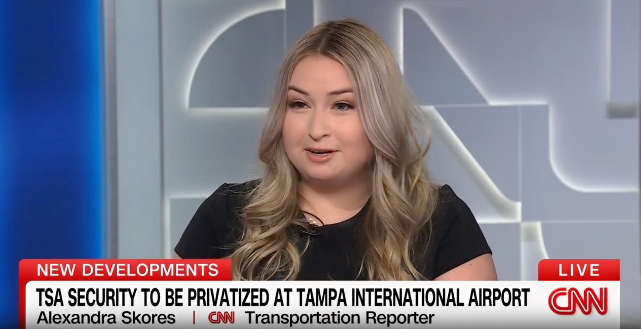 A woman with long blonde hair and a black shirt speaking during a news interview inside a studio with a blue and gray background that has a logo or design on the wall. The news banner at the bottom mentions TSA security privatization at Tampa International Airport, and her name is Alexandra Skores, a CNN transportation reporter.