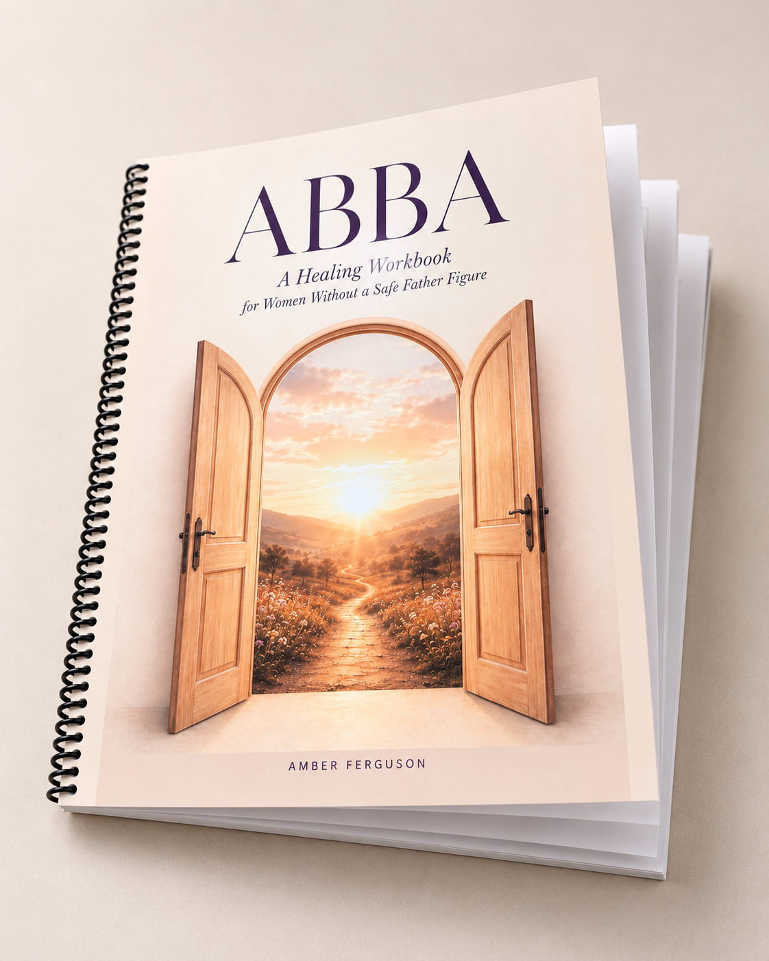 A spiral-bound workbook titled 'ABBA: A Healing Workbook for Women Without a Safe Father Figure' with a cover illustration of open wooden doors revealing a landscape with a walking path, trees, and a sunset sky.