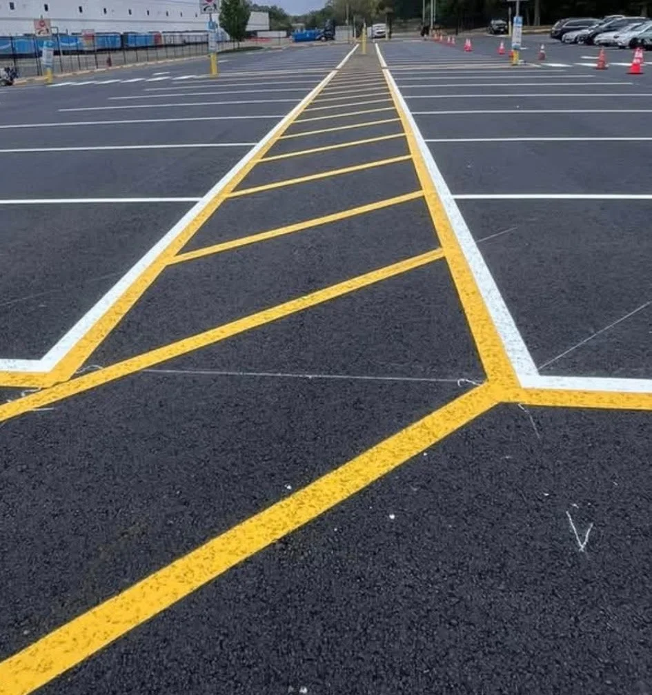 A parking lot with marked yellow striped zones for no parking, and empty spaces for parking cars. Orange cones are visible in the background.