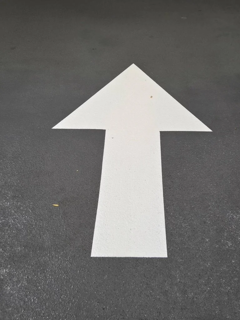 White arrow painted on dark asphalt pointing upward.