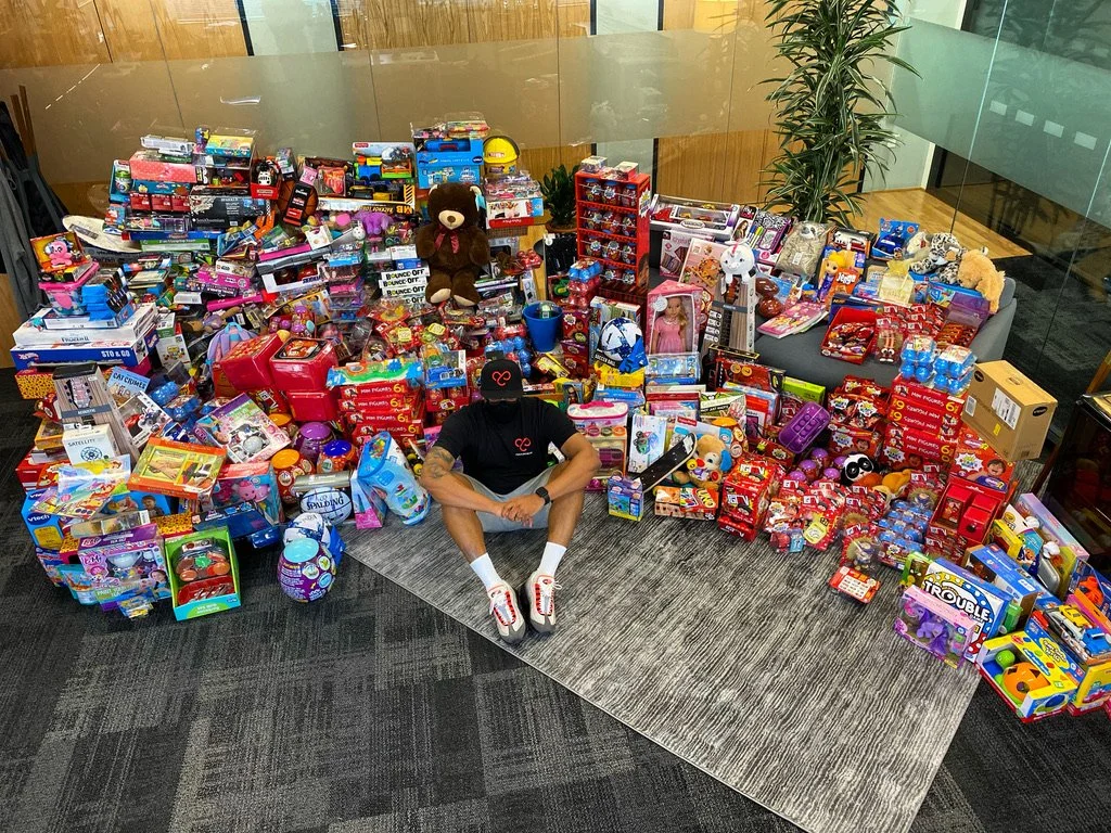 Person sitting on the floor surrounded by a large collection of toys including stuffed animals, board games, and colorful boxed toys.