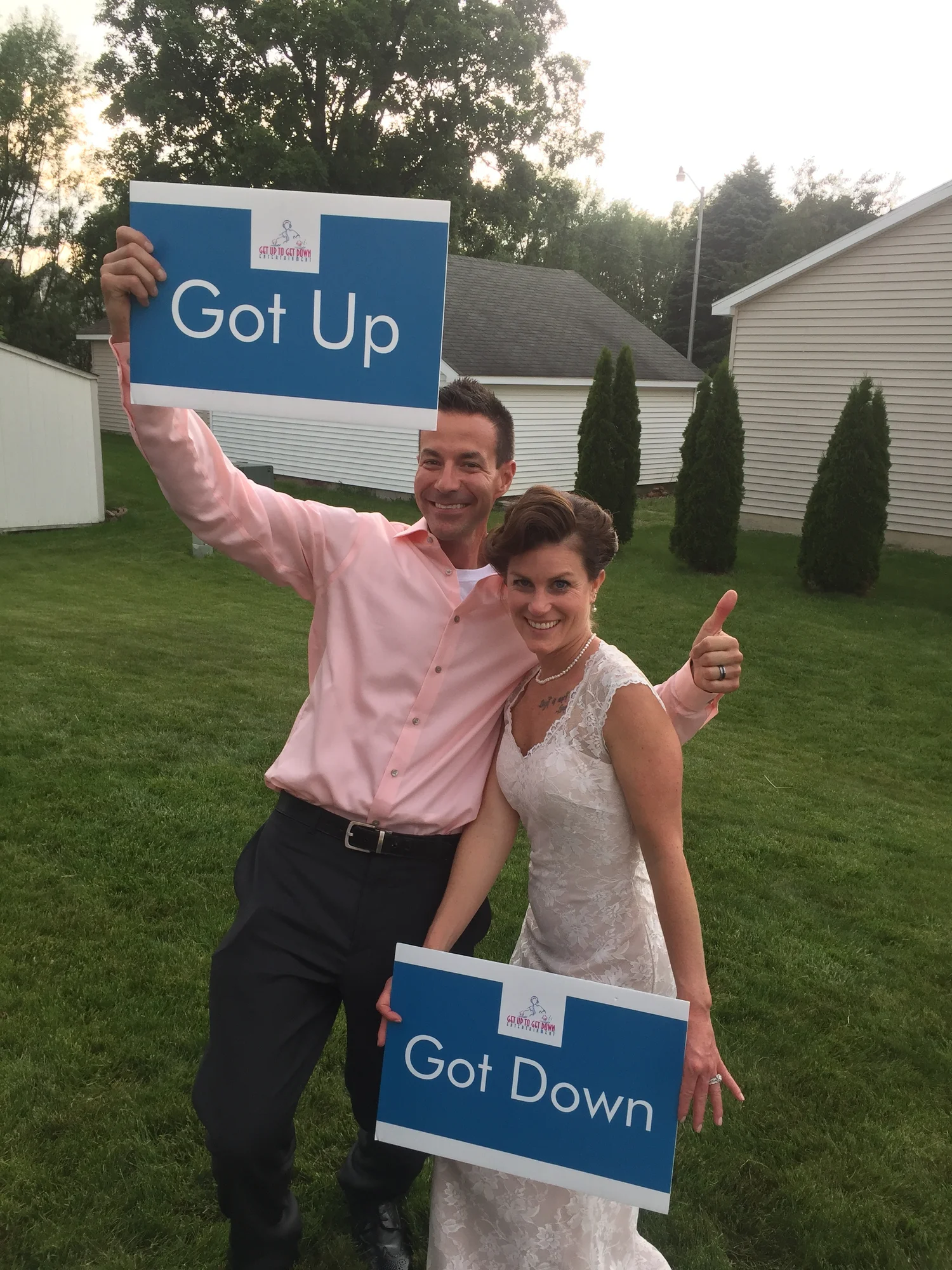 Bride and groom holding Got Up and Got Down signs on a lawn at their outdoor wedding.