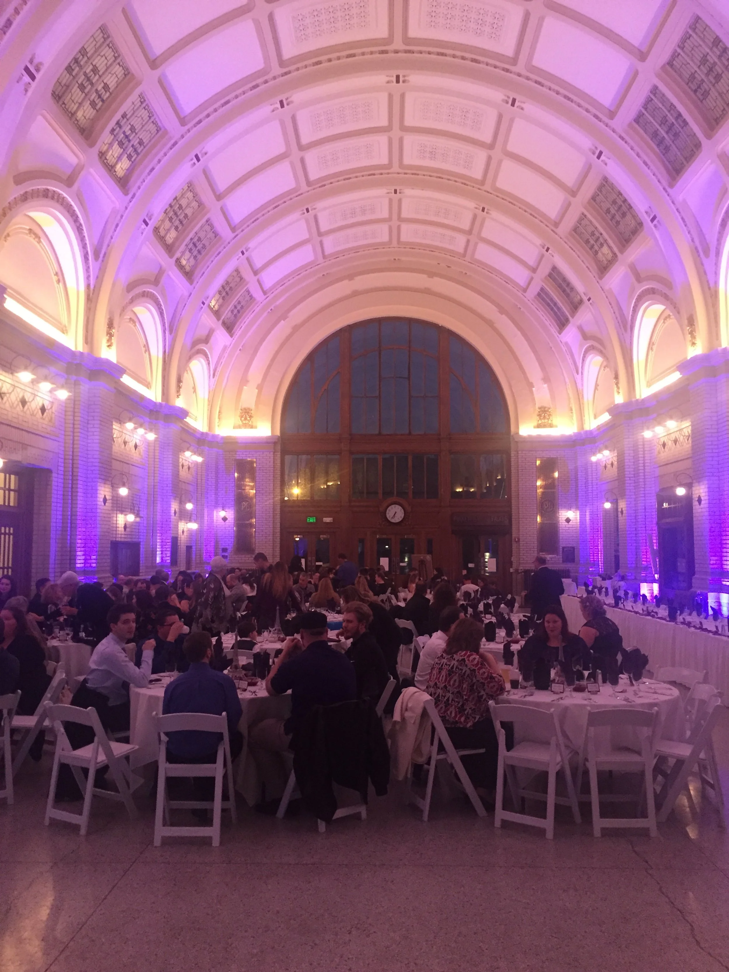 Guests seated beneath a vaulted ceiling with purple uplighting around the reception hall.