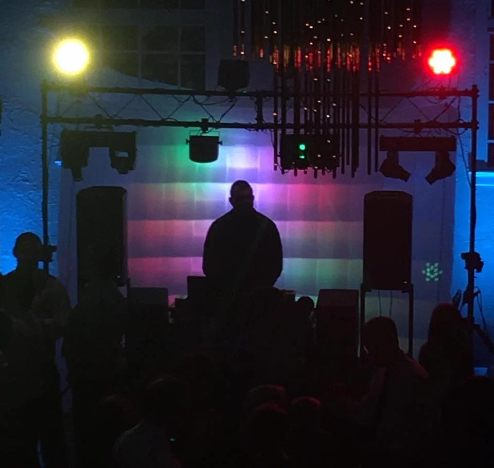 DJ silhouetted beneath a lighting truss at a wedding reception.