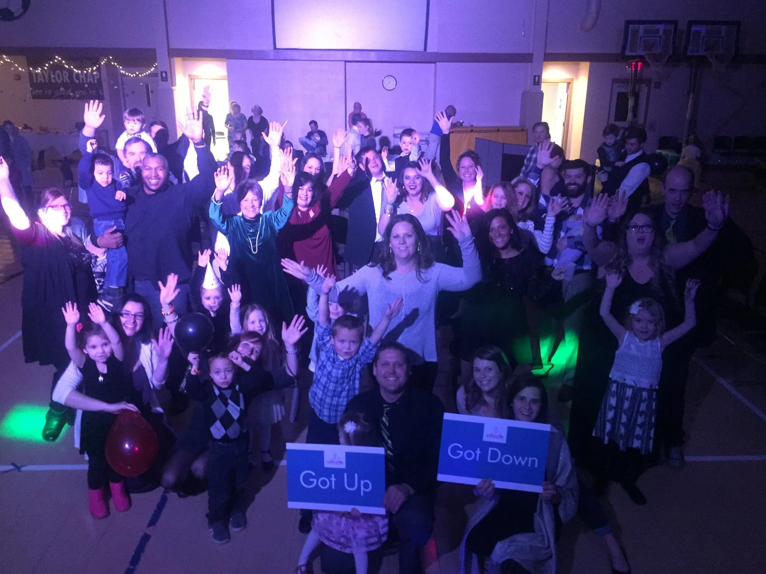Children and adults waving and holding Got Up and Got Down signs at a preschool dance.