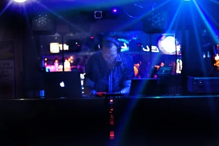 DJ wearing headphones while adjusting the mixer beneath blue stage lighting.
