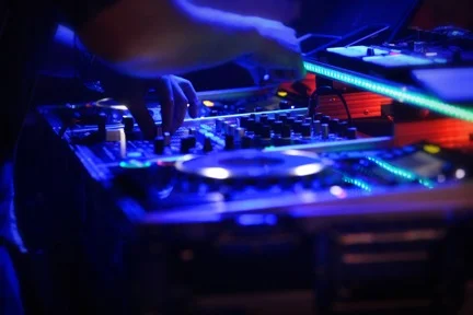 DJ hands adjusting a mixer between illuminated turntables.