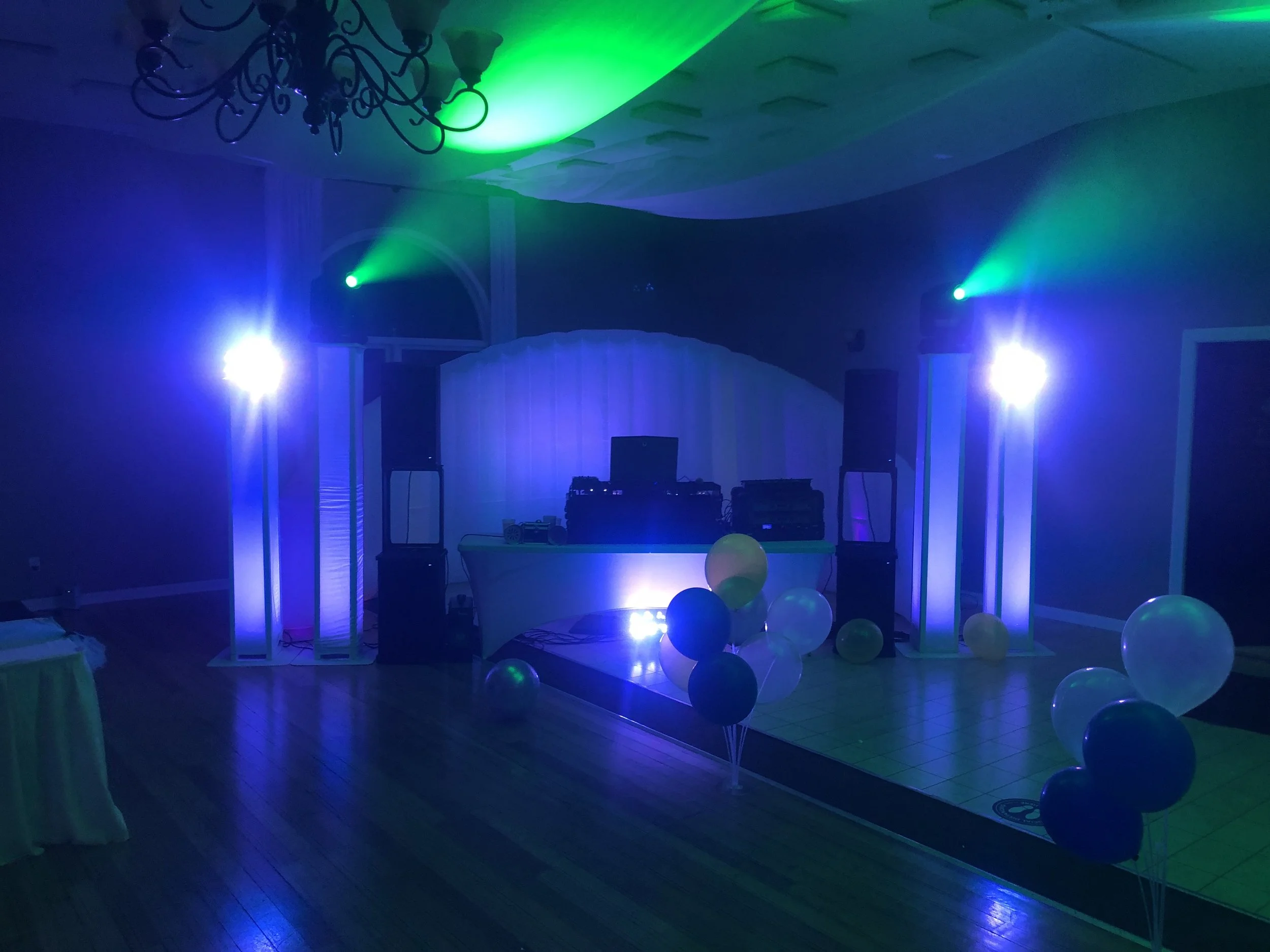 DJ booth and lighting towers casting blue and green beams across a balloon-decorated dance floor.