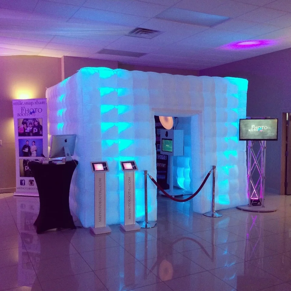 Inflatable photo booth glowing blue beside a prop table and rope barrier.