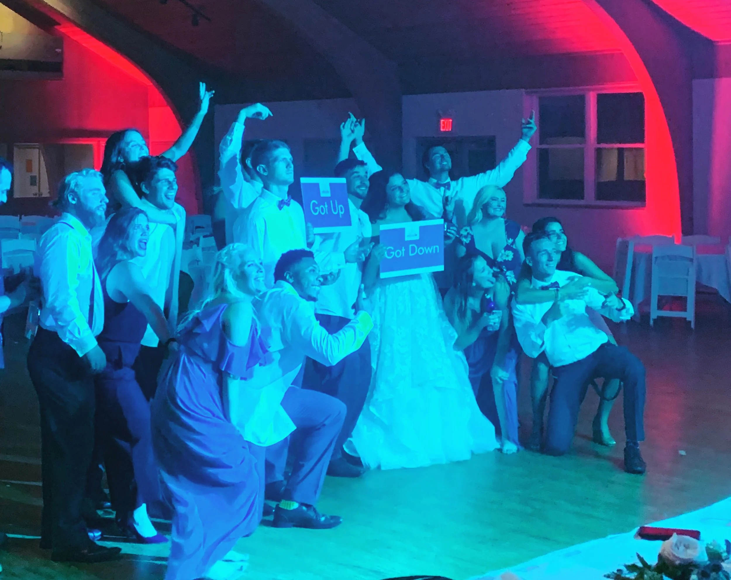 Bride and wedding guests raising their hands for a group photo under blue and red lighting.